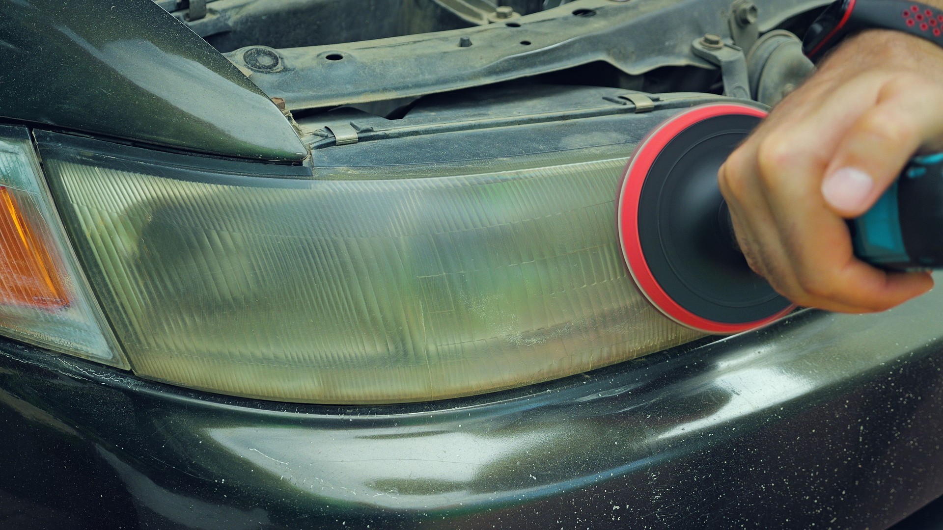 Close-up of a man using an electric drill with a polishing attachment to restore a cloudy and discolored car headlight. Polishing improves the clarity and appearance of the headlight.